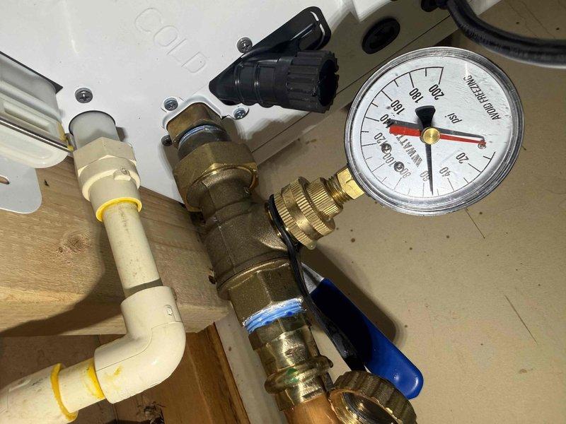 Responded to service call for tankless water heater making loud noise and toilet flush issue. Inspected recently installed tankless unit with complete plumbing assembly including pressure relief system, isolation valves, and pressure gauge. Performed system flush on tankless water heater to address noise concerns and verified proper operation of all connected components including blue-handled isolation valves and pressure regulation equipment. Documented installation configuration showing proper mounting, venting through metallic flex ductwork, and appropriate safety equipment including collection bucket beneath unit.