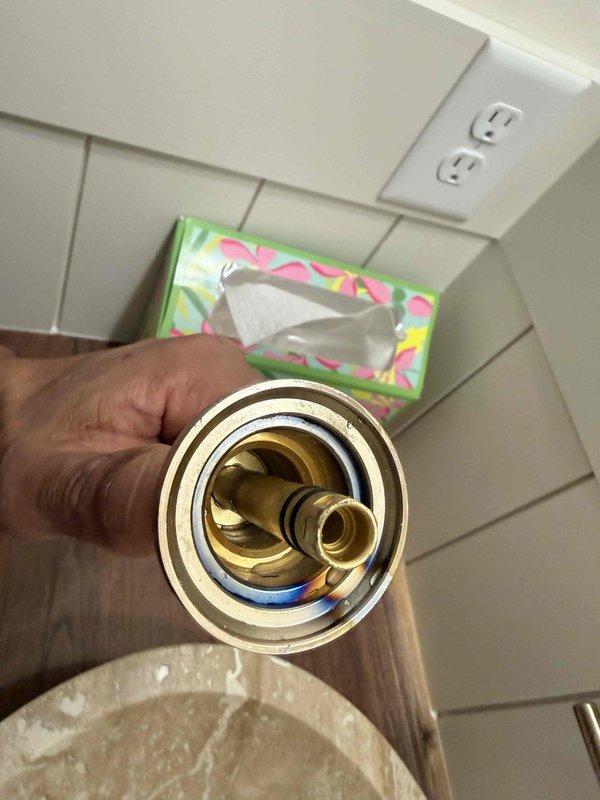 Responded to fixture inspection request and examined shower valve assembly. Found brass shower valve trim piece removed from wall, exposing threaded cartridge mechanism and central stub-out between two control handles. Documented current condition of incomplete installation showing exposed brass valve connection point with missing escutcheon plate on white subway tile wall.