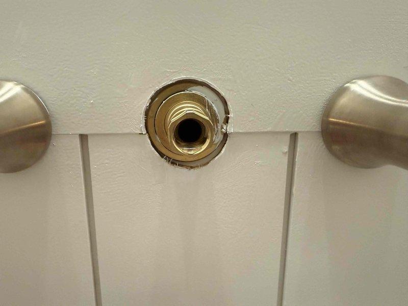 Responded to fixture inspection request and examined shower valve assembly. Found brass shower valve trim piece removed from wall, exposing threaded cartridge mechanism and central stub-out between two control handles. Documented current condition of incomplete installation showing exposed brass valve connection point with missing escutcheon plate on white subway tile wall.