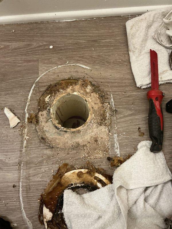 Responded to toilet flange repair request in apartment unit. Upon inspection, found cracked toilet flange with visible water damage and staining on surrounding flooring. Removed existing toilet, replaced damaged flange with new PVC flange, and reinstalled toilet with new wax ring and hardware to ensure proper seal and prevent future leaks.