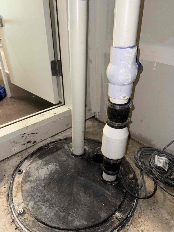 Responded to customer report of intermittent toilet clogging in basement. Upon inspection, discovered the issue was related to the sump pump system rather than the toilet itself. The sump pump pit cover and check valve assembly showed significant accumulation of debris, sediment, and mineral deposits that were affecting proper drainage function. Documented the condition of the sump pump installation, including the PVC discharge pipe configuration with multiple connections and the heavily soiled pit cover with clogged check valve dome. Advised customer that the drainage issues were likely caused by compromised sump pump performance due to lack of maintenance and recommended thorough cleaning of the pit, check valve replacement, and verification of proper pump operation to restore normal basement plumbing function.