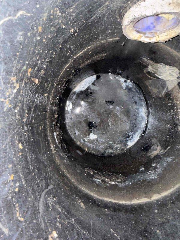 Responded to customer report of intermittent toilet clogging in basement. Upon inspection, discovered the issue was related to the sump pump system rather than the toilet itself. The sump pump pit cover and check valve assembly showed significant accumulation of debris, sediment, and mineral deposits that were affecting proper drainage function. Documented the condition of the sump pump installation, including the PVC discharge pipe configuration with multiple connections and the heavily soiled pit cover with clogged check valve dome. Advised customer that the drainage issues were likely caused by compromised sump pump performance due to lack of maintenance and recommended thorough cleaning of the pit, check valve replacement, and verification of proper pump operation to restore normal basement plumbing function.
