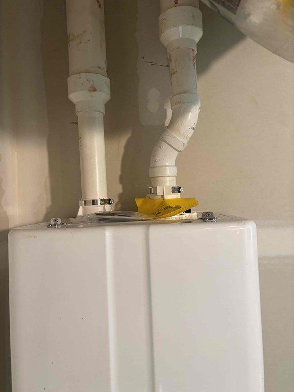 Completed installation of tankless water heater system with proper venting configuration. Installed unit on interior wall with two white PVC intake and exhaust vent pipes extending vertically through exterior wall connection, secured all plumbing connections with metal hose clamps, and verified proper mounting and operational functionality of the energy-efficient water heating system.