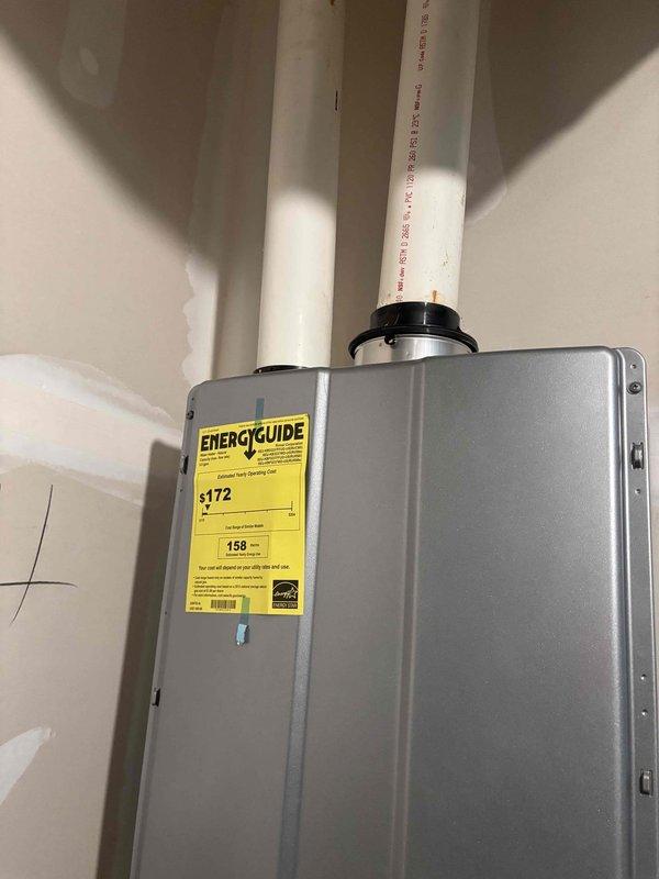 Completed installation of tankless water heater system with proper venting configuration. Installed unit on interior wall with two white PVC intake and exhaust vent pipes extending vertically through exterior wall connection, secured all plumbing connections with metal hose clamps, and verified proper mounting and operational functionality of the energy-efficient water heating system.