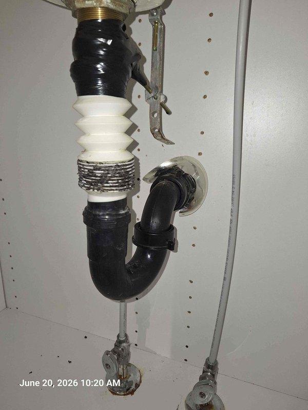 Responded to service call for leak under bathroom sink with possible obstruction in p-trap from dropped dental crown. Upon inspection, identified deteriorated flexible corrugated drain connector as source of leak. The white accordion-style flex pipe showed signs of wear at threaded connections. Documented existing plumbing configuration including P-trap assembly, black plastic piping, and metal mounting hardware. Also noted unrelated ceiling fixture above area displaying severe corrosion and water damage, indicating potential separate leak source requiring attention. Provided customer with documentation of findings and recommended replacement of compromised drain components and investigation of ceiling moisture issue.