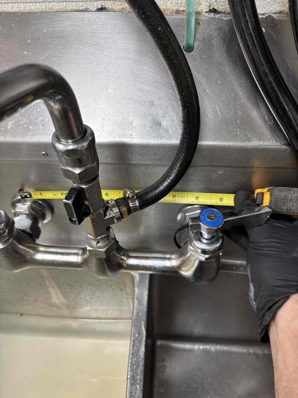 # Leak Repair - Commercial Dishwasher Area

Responded to service call for multiple leaks in commercial dishpit area. Upon arrival, conducted thorough inspection of plumbing system and identified two leak sources requiring immediate attention.

**Primary Leak Location:**
Inspected chrome-plated supply line assembly with associated valve connections. Found active leak at pipe joint connection near service valve with blue indicator cap. Leak was caused by deteriorated gasket and loose connection at fitting. Shut off water supply to affected area and disassembled connection. Replaced worn gasket, cleaned mating surfaces, and reassembled connection with proper torque specifications. Verified black foam insulation was intact and repositioned to prevent future moisture accumulation.

**Secondary Leak Location:**
Examined older cast iron valve assembly with copper pipe connections showing significant corrosion and surface deterioration. Identified leak originating from threaded port connection
