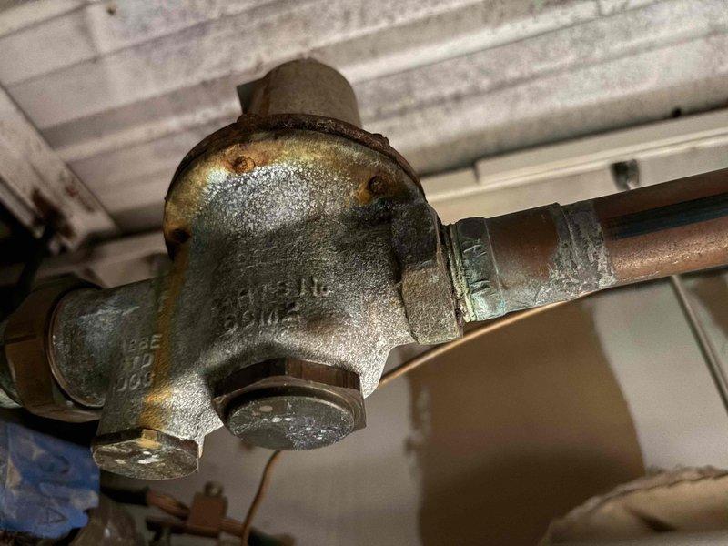 # Leak Repair - Commercial Dishwasher Area

Responded to service call for multiple leaks in commercial dishpit area. Upon arrival, conducted thorough inspection of plumbing system and identified two leak sources requiring immediate attention.

**Primary Leak Location:**
Inspected chrome-plated supply line assembly with associated valve connections. Found active leak at pipe joint connection near service valve with blue indicator cap. Leak was caused by deteriorated gasket and loose connection at fitting. Shut off water supply to affected area and disassembled connection. Replaced worn gasket, cleaned mating surfaces, and reassembled connection with proper torque specifications. Verified black foam insulation was intact and repositioned to prevent future moisture accumulation.

**Secondary Leak Location:**
Examined older cast iron valve assembly with copper pipe connections showing significant corrosion and surface deterioration. Identified leak originating from threaded port connection