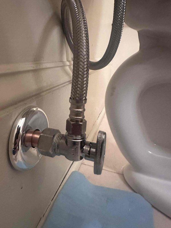 Replaced defective toilet stop valve with new chrome angle stop valve and installed new braided stainless steel flexible supply line. Verified proper water flow and tested for leaks to ensure reliable operation of wall-mounted toilet tank system.