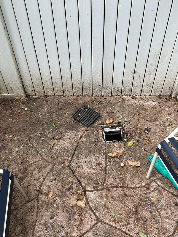 Responded to clogged drain service call for backyard and side yard drainage systems suspected of root intrusion. Inspected square metal drainage grates in lawn area and patio, accessing underground drainage components through utility access panel. Assessed condition of drain lines and documented existing blockages caused by root infiltration in outdoor drainage system.