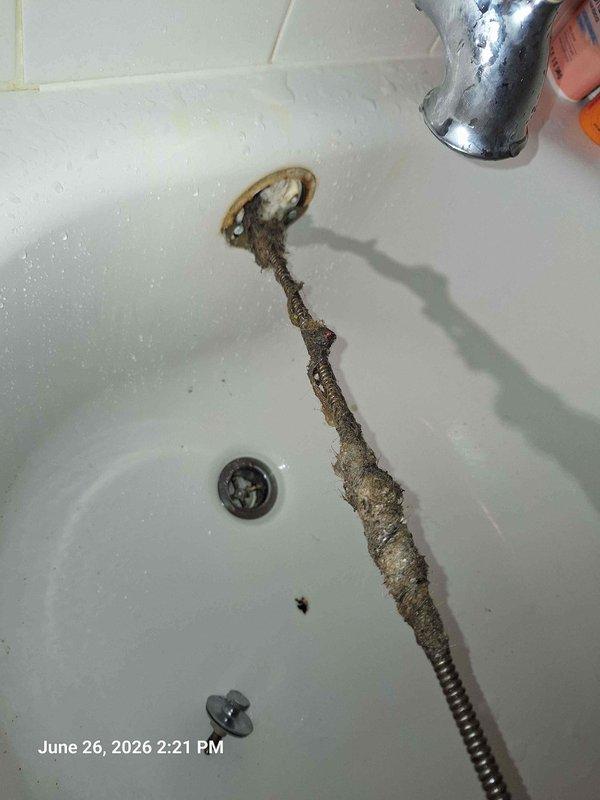 Responded to service call for dishwasher water line connection and slow-draining bathtub. Upon inspection, discovered severely corroded and deteriorated flexible shower hose in bathtub with extensive mineral buildup and corrosion requiring replacement. Assessed kitchen area where dishwasher installation was requested, noting exposed electrical wiring with wire connectors in place and cabinetry configuration for appliance hookup. Documented existing plumbing conditions including tub drain assembly and fixtures for necessary repairs to restore proper drainage function.