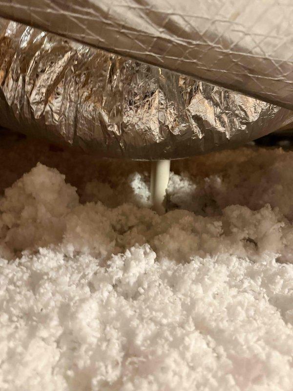 Responded to report of wet spot below bathroom and laundry room. Conducted thorough inspection of attic space above affected areas to identify source of moisture intrusion. Located evidence of active water damage on wooden structural support beam, exhibiting significant moisture saturation, discoloration, and deterioration consistent with prolonged water exposure. Observed orange-brown rot pattern with compromised wood fibers and dark moisture staining on upper section of support member. 

Traced leak source by examining plumbing lines, HVAC components, and building envelope in vicinity of damaged structural element. Inspected flexible aluminum HVAC ductwork in attic space, noting exterior foil wrap damage and separation in multiple locations. Assessed insulation conditions surrounding affected area and documented extent of moisture penetration. 

Photographed damaged structural beam showing active deterioration and water intrusion evidence. Documented HVAC ductwork condition and surro