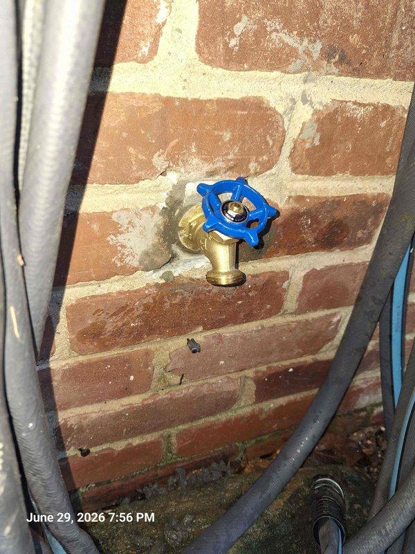 Responded to leak at exterior shut off valve. Upon arrival, restoration company was already on site addressing water damage. Inspected outdoor hose bib with blue cross-handle mounted on brick exterior wall and traced supply line to interior shut off valve assembly. 

Found active leak at interior shut off valve connection point within wall cavity. Exposed plumbing system revealed corroded valve components and compromised brass fittings on copper supply lines. Shut off water supply, documented existing conditions including water separator/filter unit and deteriorated valve hardware showing signs of age and mineral buildup. Photographed interior plumbing configuration with exposed copper piping, brass connections, and moisture barrier for insurance documentation purposes.