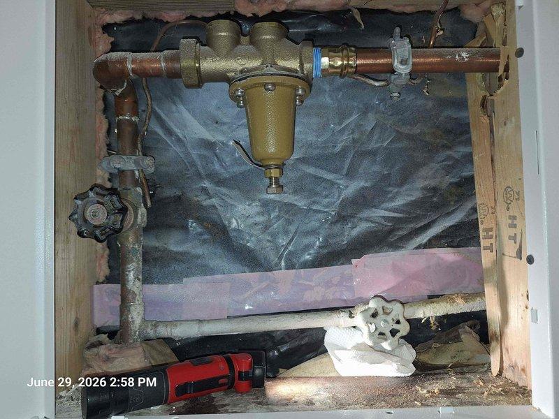 Responded to leak at exterior shut off valve. Upon arrival, restoration company was already on site addressing water damage. Inspected outdoor hose bib with blue cross-handle mounted on brick exterior wall and traced supply line to interior shut off valve assembly. 

Found active leak at interior shut off valve connection point within wall cavity. Exposed plumbing system revealed corroded valve components and compromised brass fittings on copper supply lines. Shut off water supply, documented existing conditions including water separator/filter unit and deteriorated valve hardware showing signs of age and mineral buildup. Photographed interior plumbing configuration with exposed copper piping, brass connections, and moisture barrier for insurance documentation purposes.