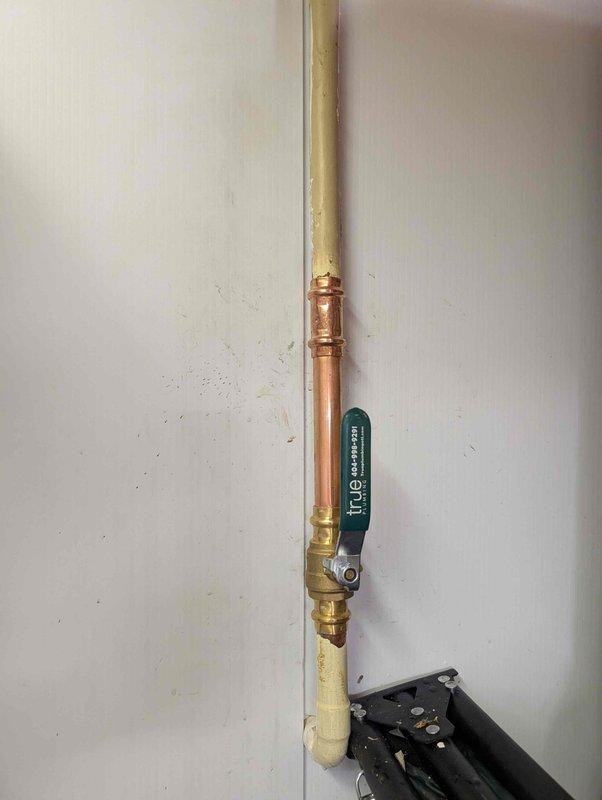 Responded to leak at pressure reducing valve (PRV) assembly. Upon inspection, identified active leak at brass fittings on vertical copper pipe assembly with ball valve connection. Assessed PRV installation including associated T-fittings and copper piping with decorative ridged section. Inspected crawl space area above to verify no water damage to ceiling joists, insulation, or surrounding infrastructure. Documented condition of plumbing assembly showing normal patina on copper and brass components with minor wall staining from moisture exposure. Photographed PRV configuration and overhead plumbing runs for service records. Completed leak repair at fitting connections and verified system integrity.