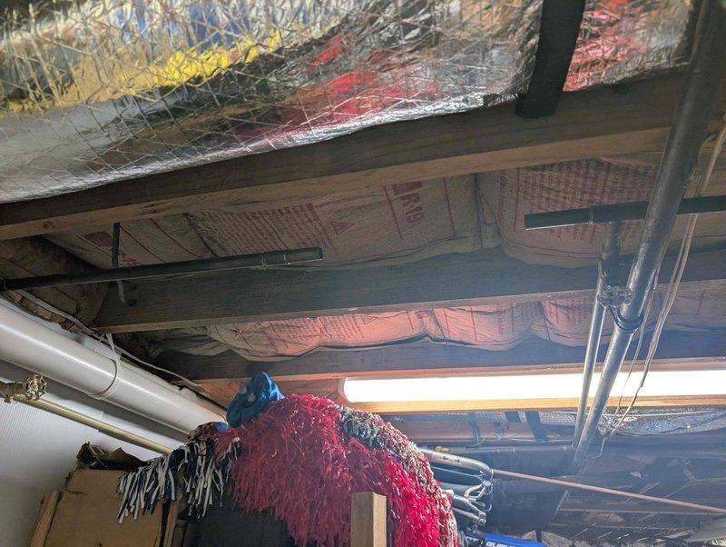 Responded to leak at pressure reducing valve (PRV) assembly. Upon inspection, identified active leak at brass fittings on vertical copper pipe assembly with ball valve connection. Assessed PRV installation including associated T-fittings and copper piping with decorative ridged section. Inspected crawl space area above to verify no water damage to ceiling joists, insulation, or surrounding infrastructure. Documented condition of plumbing assembly showing normal patina on copper and brass components with minor wall staining from moisture exposure. Photographed PRV configuration and overhead plumbing runs for service records. Completed leak repair at fitting connections and verified system integrity.