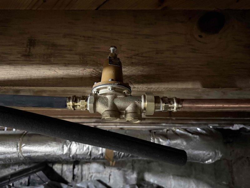 Completed follow-up service call to address high water pressure concerns following recent water service repair. Inspected and photographed the existing pressure reducing valve installation located in the crawlspace beneath the structure. The brass pressure reducing valve with adjustment mechanism was found properly installed on the copper water line with secure compression fittings on both inlet and outlet connections. Valve was mounted to floor joists using appropriate support strapping to prevent stress on pipe connections. All components appeared to be functioning as designed with no visible leaks or defects noted at the time of inspection.