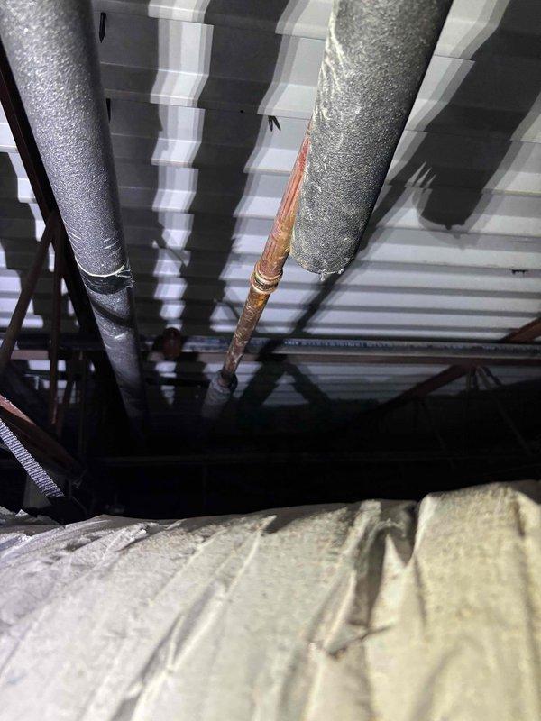 Completed repair of 1-inch copper refrigerant line in attic space showing significant corrosion and oxidation. Located damaged section of copper piping running between insulated HVAC ducts where moisture infiltration had caused deterioration and active condensation drip. Cut out compromised section of copper line, installed new copper pipe segment, and brazed connections to restore system integrity. Verified proper insulation placement around repair area and confirmed no additional leaks present.