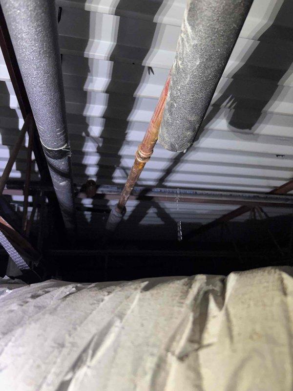 Completed repair of 1-inch copper refrigerant line in attic space showing significant corrosion and oxidation. Located damaged section of copper piping running between insulated HVAC ducts where moisture infiltration had caused deterioration and active condensation drip. Cut out compromised section of copper line, installed new copper pipe segment, and brazed connections to restore system integrity. Verified proper insulation placement around repair area and confirmed no additional leaks present.