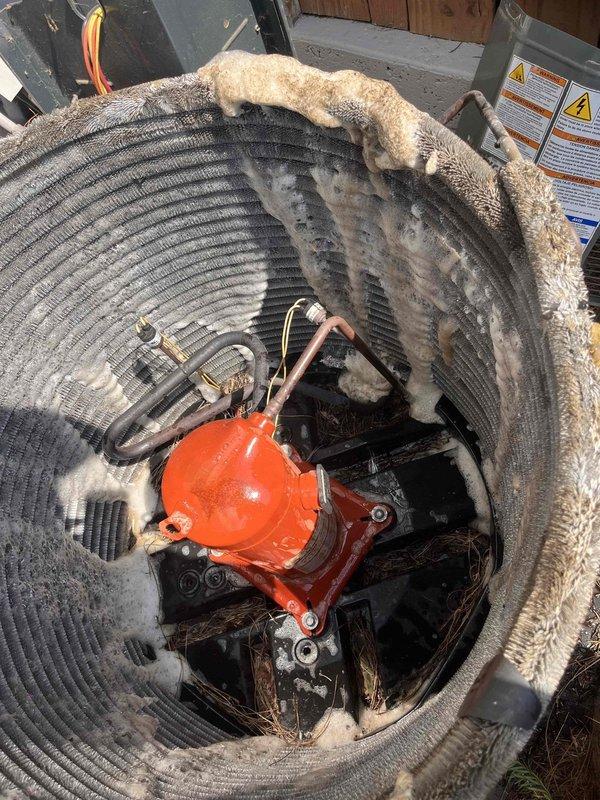 Responded to no cooling call on 11-year-old dual zone townhome system. Upon arrival, found cylindrical outdoor condensing unit with severe debris accumulation and lack of maintenance. Condenser coil heavily restricted with thick buildup of lint, fiber material, dust, and organic debris throughout fins and coil surfaces. Performed thorough coil cleaning to remove all contaminants and restore proper airflow through unit. Verified system operation and cooling performance after cleaning. Unit returned to normal operation with adequate airflow and refrigerant circuit function restored.