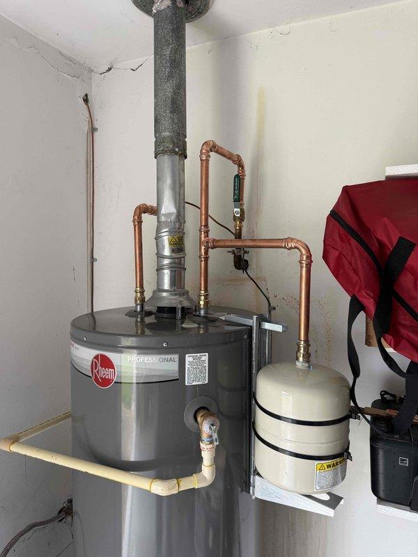 # Water Heater Expansion Tank Replacement and Pressure Regulation
Responded to service call for leaking expansion tank and elevated water pressure on residential water heater system. Upon arrival, performed visual inspection of Rheem water heater and associated plumbing components.
## Issues Identified
Confirmed expansion tank failure with active leak at tank connection point. Pressure gauge reading indicated system pressure exceeding recommended operating range, measuring above safe threshold on ProLine gauge mounted at water heater inlet. Excessive pressure contributing to expansion tank failure and potential risk to water heater integrity.
## Work Performed
- Shut off water supply to water heater system
- Drained and depressurized existing failed expansion tank
- Removed compromised expansion tank from wall-mounted bracket
- Installed new white cylindrical expansion tank with proper sizing for system capacity
- Secured expansion tank to wall using black mounting straps for stab # Water Heater Expansion Tank Replacement and Pressure Regulation
Responded to service call for leaking expansion tank and elevated water pressure on residential water heater system. Upon arrival, performed visual inspection of Rheem water heater and associated plumbing components.
## Issues Identified
Confirmed expansion tank failure with active leak at tank connection point. Pressure gauge reading indicated system pressure exceeding recommended operating range, measuring above safe threshold on ProLine gauge mounted at water heater inlet. Excessive pressure contributing to expansion tank failure and potential risk to water heater integrity.
## Work Performed
- Shut off water supply to water heater system
- Drained and depressurized existing failed expansion tank
- Removed compromised expansion tank from wall-mounted bracket
- Installed new white cylindrical expansion tank with proper sizing for system capacity
- Secured expansion tank to wall using black mounting straps for stab