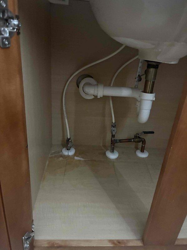 Arrived on-site at 11:30 to assess bathroom vanity plumbing configuration. Documented existing under-sink plumbing installation including white PVC P-trap drain assembly, flexible supply lines, chrome shut-off valves mounted on cabinet floor, and all associated connections and fittings in proper working condition.
