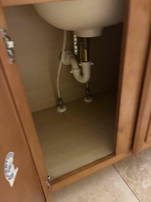 Arrived on-site at 11:30 to assess bathroom vanity plumbing configuration. Documented existing under-sink plumbing installation including white PVC P-trap drain assembly, flexible supply lines, chrome shut-off valves mounted on cabinet floor, and all associated connections and fittings in proper working condition.