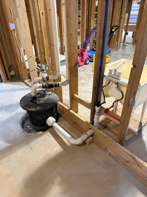 Assessed existing sump pump installation in basement requiring relocation to lower depth within concrete floor. Inspected rough-in plumbing stub-outs throughout basement framing to verify viability for future fixture connections. Evaluated black sewage ejector pump system with associated PVC discharge piping and documented current configuration including horizontal runs and vertical penetrations through wall framing. Confirmed water supply rough-in with PEX tubing and drainage system routing during active construction phase. Assessed existing sump pump installation in basement requiring relocation to lower depth within concrete floor. Inspected rough-in plumbing stub-outs throughout basement framing to verify viability for future fixture connections. Evaluated black sewage ejector pump system with associated PVC discharge piping and documented current configuration including horizontal runs and vertical penetrations through wall framing. Confirmed water supply rough-in with PEX tubing and drainage system routing during active construction phase.