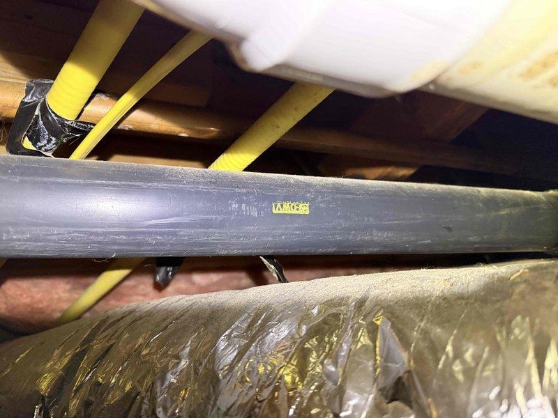 # Leak Investigation and Assessment
Responded to report of ceiling leak and conducted thorough inspection of attic space above affected area. Located source of water intrusion at PVC drain line running through attic crawl space. Documented condition of plumbing system, including gray PVC piping secured with yellow support straps to wooden joists, and adjacent HVAC ductwork.
Inspection revealed significant water damage to structural floor joist beneath leak point. Wood member exhibited dark staining and deterioration along edge, indicating prolonged moisture exposure. Damage pattern consistent with slow leak from overhead plumbing. Photographed compromised structural element, noting discoloration ranging from natural wood tone to dark brown/black staining where rot had begun. White flexible ductwork and pink insulation also visible in affected area.
Assessment confirmed active leak requiring plumbing repair and subsequent evaluation of damaged structural framing for potential reinfor # Leak Investigation and Assessment
Responded to report of ceiling leak and conducted thorough inspection of attic space above affected area. Located source of water intrusion at PVC drain line running through attic crawl space. Documented condition of plumbing system, including gray PVC piping secured with yellow support straps to wooden joists, and adjacent HVAC ductwork.
Inspection revealed significant water damage to structural floor joist beneath leak point. Wood member exhibited dark staining and deterioration along edge, indicating prolonged moisture exposure. Damage pattern consistent with slow leak from overhead plumbing. Photographed compromised structural element, noting discoloration ranging from natural wood tone to dark brown/black staining where rot had begun. White flexible ductwork and pink insulation also visible in affected area.
Assessment confirmed active leak requiring plumbing repair and subsequent evaluation of damaged structural framing for potential reinfor