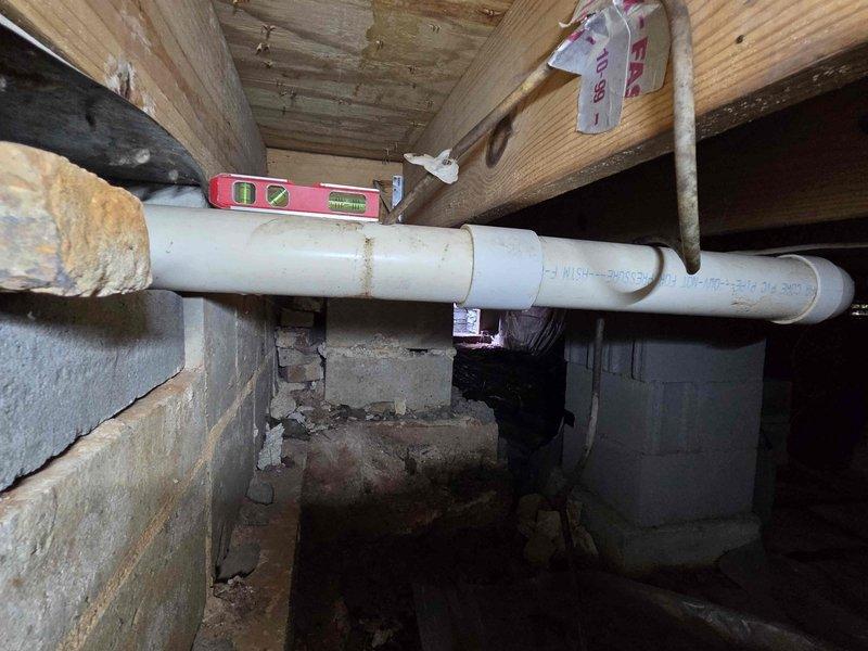 Responded to clogged toilet with backup occurring in laundry room on opposite side of ranch-style home. Accessed crawl space and inspected drainage system, identifying blockage in main drain line. Cleared obstruction in horizontal PVC drain pipe running beneath floor joists, verified proper slope using level, and confirmed drainage flow was restored to both toilet and laundry room fixtures. Responded to clogged toilet with backup occurring in laundry room on opposite side of ranch-style home. Accessed crawl space and inspected drainage system, identifying blockage in main drain line. Cleared obstruction in horizontal PVC drain pipe running beneath floor joists, verified proper slope using level, and confirmed drainage flow was restored to both toilet and laundry room fixtures.