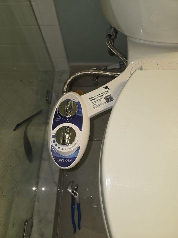 Removed existing bidet attachment and installed new customer-supplied bidet unit on toilet fixture. Connected braided metal supply hose to water supply line, mounted control panel with dual chrome dials and adjustment buttons on left side of toilet, and verified all plumbing connections were secure and leak-free. Removed existing bidet attachment and installed new customer-supplied bidet unit on toilet fixture. Connected braided metal supply hose to water supply line, mounted control panel with dual chrome dials and adjustment buttons on left side of toilet, and verified all plumbing connections were secure and leak-free.