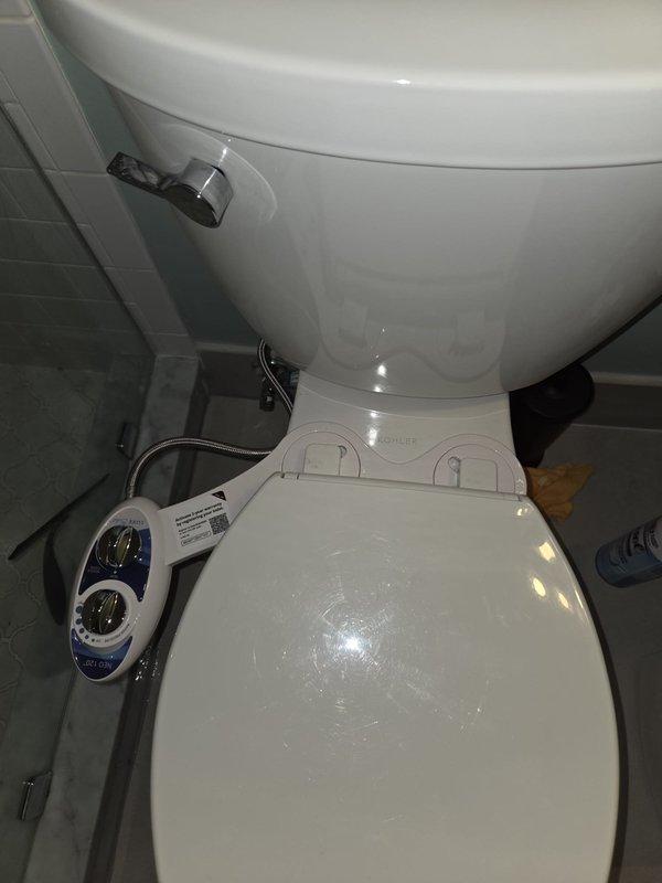 Removed existing bidet attachment and installed new customer-supplied bidet unit on toilet fixture. Connected braided metal supply hose to water supply line, mounted control panel with dual chrome dials and adjustment buttons on left side of toilet, and verified all plumbing connections were secure and leak-free. Removed existing bidet attachment and installed new customer-supplied bidet unit on toilet fixture. Connected braided metal supply hose to water supply line, mounted control panel with dual chrome dials and adjustment buttons on left side of toilet, and verified all plumbing connections were secure and leak-free.