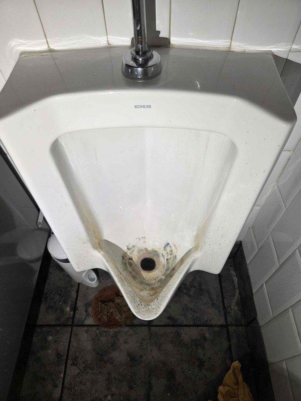 Responded to commercial restroom for reported urinal clog. Upon arrival, inspected wall-mounted Kohler urinal and identified drainage obstruction preventing proper water flow. Cleared blockage using appropriate drain cleaning equipment and restored full drainage function. Tested flush valve operation and verified complete water evacuation through drain system. Noted mineral deposits and staining around drain connection point indicating long-term moisture issues. Advised facility maintenance of condition and recommended regular preventative maintenance to minimize future clogs. Responded to commercial restroom for reported urinal clog. Upon arrival, inspected wall-mounted Kohler urinal and identified drainage obstruction preventing proper water flow. Cleared blockage using appropriate drain cleaning equipment and restored full drainage function. Tested flush valve operation and verified complete water evacuation through drain system. Noted mineral deposits and staining around drain connection point indicating long-term moisture issues. Advised facility maintenance of condition and recommended regular preventative maintenance to minimize future clogs.