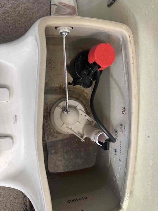 Responded to customer complaint of toilet tank refilling slowly. Upon inspection, found toilet fill valve operating at reduced flow rate. Examined tank interior and noted mineral buildup on internal components and porcelain surfaces. Inspected water supply line and angle stop valve beneath fixture for flow restrictions. Verified braided supply line and chrome shut-off valve were in good condition with no visible kinks or obstructions. Diagnosed slow fill issue as likely caused by debris or mineral deposits restricting flow through fill valve. Documented tank conditions including low water level, sediment accumulation, and discolored porcelain from hard water deposits. Photographed flush mechanism components including metal fill valve assembly, black plastic flush valve with red flapper, and overflow tube for service records. Responded to customer complaint of toilet tank refilling slowly. Upon inspection, found toilet fill valve operating at reduced flow rate. Examined tank interior and noted mineral buildup on internal components and porcelain surfaces. Inspected water supply line and angle stop valve beneath fixture for flow restrictions. Verified braided supply line and chrome shut-off valve were in good condition with no visible kinks or obstructions. Diagnosed slow fill issue as likely caused by debris or mineral deposits restricting flow through fill valve. Documented tank conditions including low water level, sediment accumulation, and discolored porcelain from hard water deposits. Photographed flush mechanism components including metal fill valve assembly, black plastic flush valve with red flapper, and overflow tube for service records.