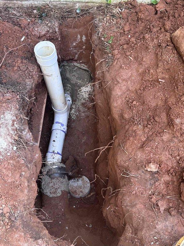 Completed installation and repair of exterior cleanout system. Excavated trench in clay soil and installed white PVC cleanout pipe with proper fittings and connections, ensuring adequate base support with stone material. Extended piping system into interior mechanical room with new vertical and horizontal PVC runs, utilizing black couplings and elbow joints to integrate with existing plumbing infrastructure. Completed installation and repair of exterior cleanout system. Excavated trench in clay soil and installed white PVC cleanout pipe with proper fittings and connections, ensuring adequate base support with stone material. Extended piping system into interior mechanical room with new vertical and horizontal PVC runs, utilizing black couplings and elbow joints to integrate with existing plumbing infrastructure.