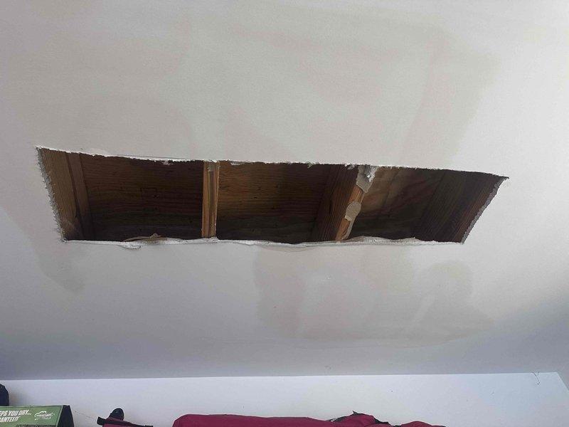 Responded to report of ceiling leak in garage area suspected to be from toilet above. Upon investigation, removed section of drywall ceiling to access plumbing and structural components. Created rectangular access opening exposing floor joists and subfloor decking to inspect for water damage and identify leak source. Documented conditions with photos showing exposed framing members and investigation area for further assessment and repair planning. Responded to report of ceiling leak in garage area suspected to be from toilet above. Upon investigation, removed section of drywall ceiling to access plumbing and structural components. Created rectangular access opening exposing floor joists and subfloor decking to inspect for water damage and identify leak source. Documented conditions with photos showing exposed framing members and investigation area for further assessment and repair planning.