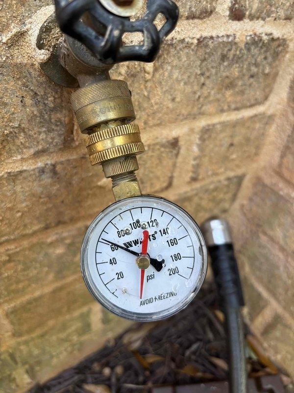 Inspected one of the dual 50-gallon gas water heaters reported as leaking and found moisture on the galvanized flue and condensation on the unit, with an expansion tank installed on the cold supply line. Tested static water pressure at an exterior hose bib using a gauge, which read approximately 60 psi, within normal range and ruling out excessive pressure as the cause of the leak. Inspected one of the dual 50-gallon gas water heaters reported as leaking and found moisture on the galvanized flue and condensation on the unit, with an expansion tank installed on the cold supply line. Tested static water pressure at an exterior hose bib using a gauge, which read approximately 60 psi, within normal range and ruling out excessive pressure as the cause of the leak.