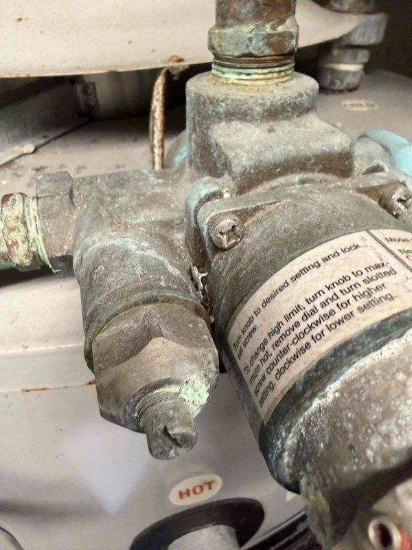 Conducted assessment for water heater replacement at Cross Ultra Lounge, documenting corroded T-valve with significant mineral buildup and oxidation on connection points. Inspection revealed an 80-gallon unit with deteriorated components and evaluated existing mechanical room configuration with copper piping showing verdigris for proper replacement planning.
