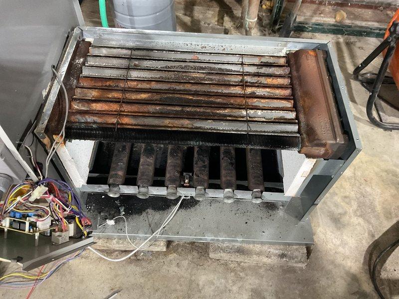 Performed maintenance service on commercial boiler system, disassembling unit to access severely corroded heat exchanger. Cleaned heat exchanger components which showed significant rust formation and soot buildup throughout the coil assembly and burner tubes, documenting condition with photos for service record.
