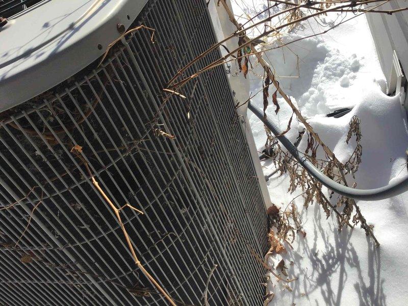 Conducted inspection of residential HVAC system during winter conditions. Observed outdoor heat pump/condenser unit with vegetation entanglement on coil grille and snow accumulation around unit. Noted proper functioning of home entry security components including door sensor mounted on frame adjacent to locking mechanisms.