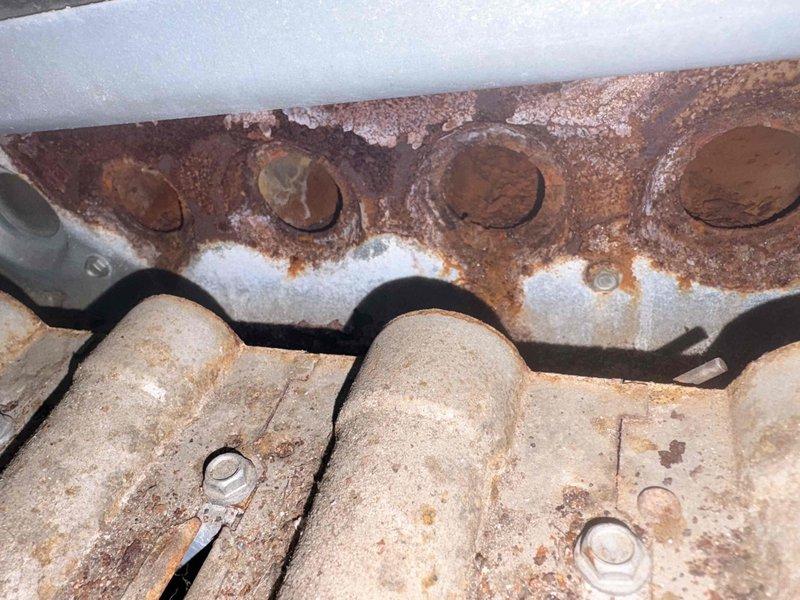 Performed warranty inspection on customer's heating system and documented extensive rust and corrosion affecting the heat exchanger and burner assembly. Photographic evidence shows severe deterioration of metal components, including manifold plate with four circular openings and connecting cylindrical components, indicating potential safety hazards and need for replacement.