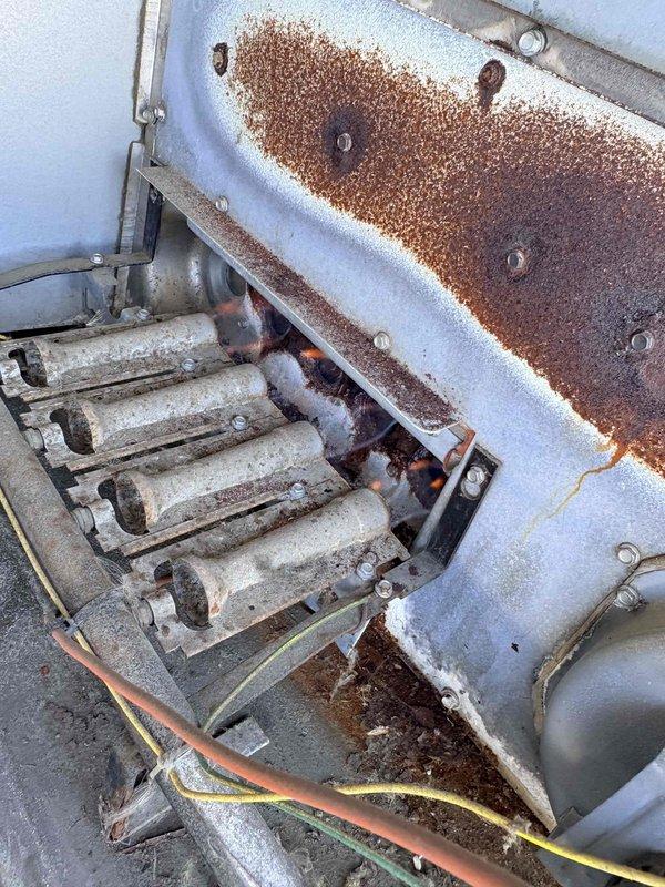 Performed warranty inspection on customer's heating system and documented extensive rust and corrosion affecting the heat exchanger and burner assembly. Photographic evidence shows severe deterioration of metal components, including manifold plate with four circular openings and connecting cylindrical components, indicating potential safety hazards and need for replacement.