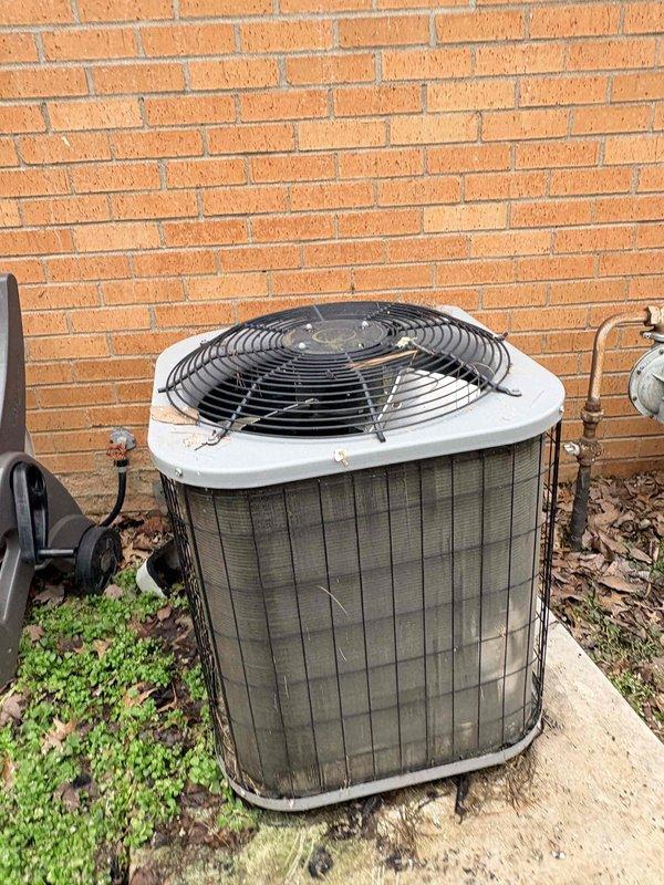 Inspected outdoor condenser unit located against brick exterior wall. Unit shows signs of age with weathered exterior, dirty coils, and general wear. Documented condition with photos showing the equipment mounted on concrete pad with nearby electrical disconnect. System appears operational but exhibits normal deterioration consistent with extended service life.