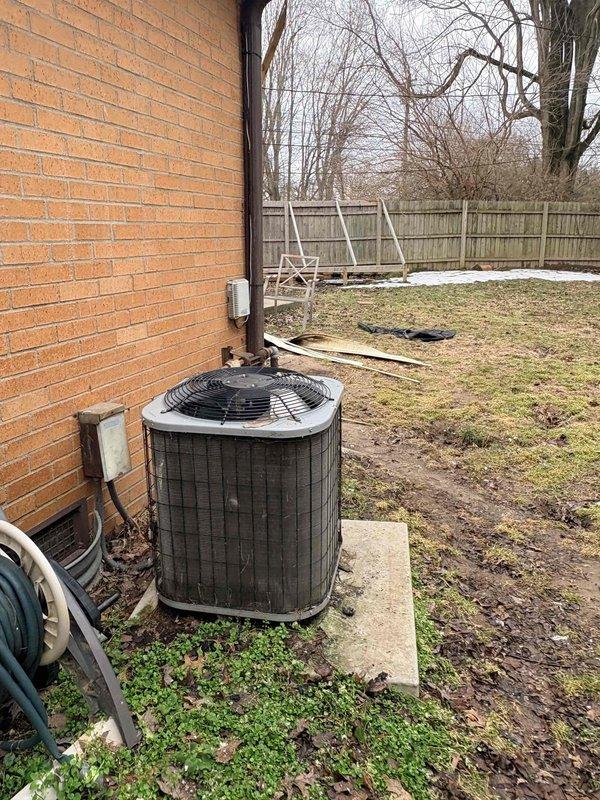 Inspected outdoor condenser unit located against brick exterior wall. Unit shows signs of age with weathered exterior, dirty coils, and general wear. Documented condition with photos showing the equipment mounted on concrete pad with nearby electrical disconnect. System appears operational but exhibits normal deterioration consistent with extended service life.