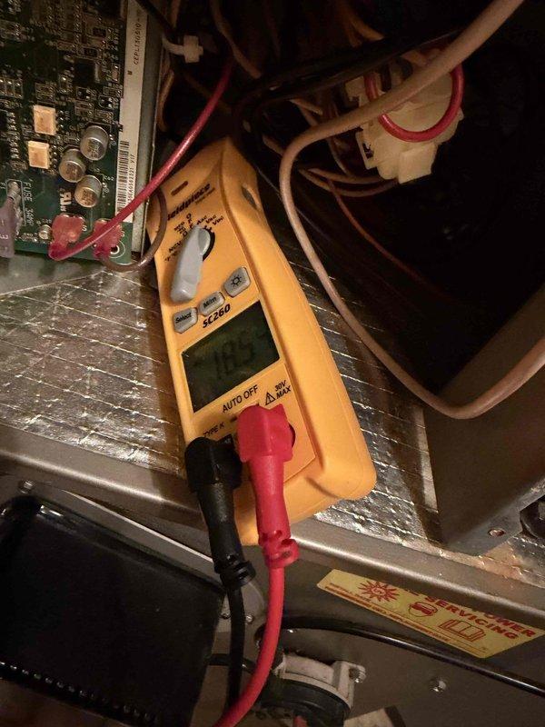 Conducted scheduled tune-up service on outdoor air conditioning condenser unit mounted against brick wall. Performed electrical system diagnostics using SC260 multimeter, which registered 182V at the control board. Inspected all components including capacitors, wiring connections and electrical harnesses, confirming proper operation of the system.