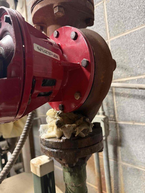 Responded to service call for middle boiler system experiencing severe leak. Inspection revealed significant corrosion at metal flange/coupling junction with extensive rust buildup. Red circulator pump showed deterioration at connection point with aged, crumbling insulation material and signs of oxidation on adjacent piping. Replaced damaged components and sealed connections to resolve the leak issue.