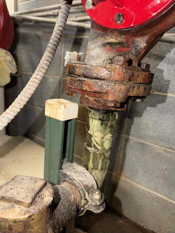 Responded to service call for middle boiler system experiencing severe leak. Inspection revealed significant corrosion at metal flange/coupling junction with extensive rust buildup. Red circulator pump showed deterioration at connection point with aged, crumbling insulation material and signs of oxidation on adjacent piping. Replaced damaged components and sealed connections to resolve the leak issue.