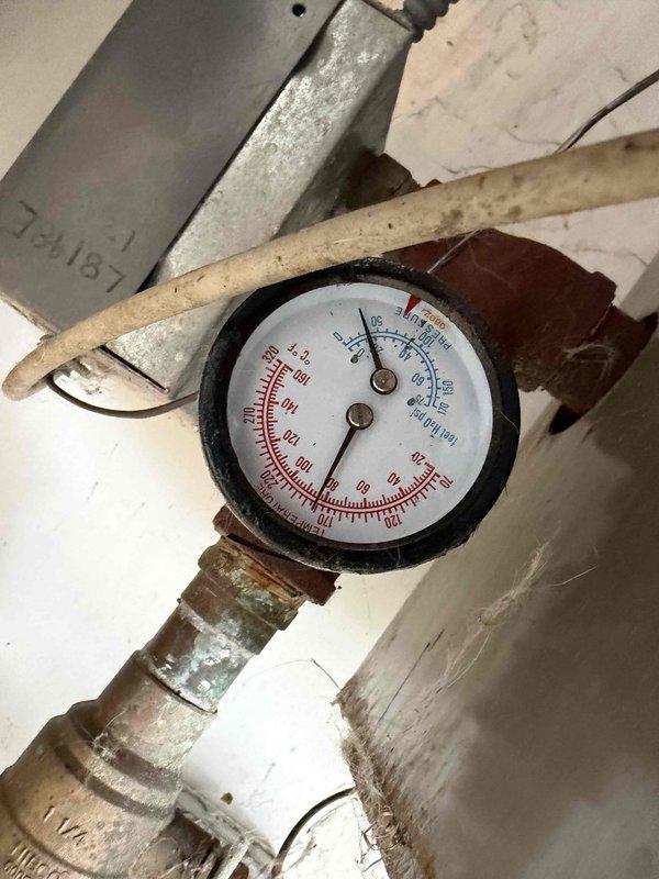 Responded to callback regarding persistent boiler leak. Inspected pressure gauge on system piping, noting low pressure reading and signs of corrosion at connection points. Examined mechanical room containing furnace, water heater tanks, and associated plumbing infrastructure to identify source of leak.