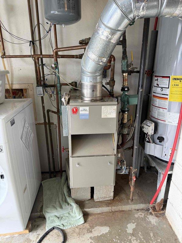 Responded to callback regarding persistent boiler leak. Inspected pressure gauge on system piping, noting low pressure reading and signs of corrosion at connection points. Examined mechanical room containing furnace, water heater tanks, and associated plumbing infrastructure to identify source of leak.