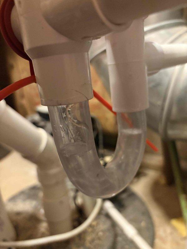 Diagnosed ongoing furnace cycling issue that has persisted since December. Inspected condensate drainage system, noting mineral buildup in the clear trap and checking connected PVC piping for proper installation. Examined wall-mounted plumbing components for potential water damage that could be affecting furnace operation.