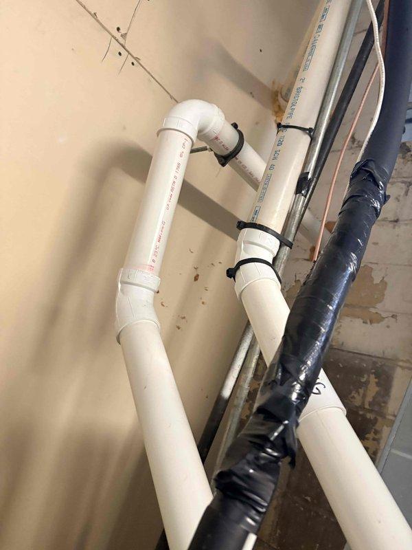 Diagnosed ongoing furnace cycling issue that has persisted since December. Inspected condensate drainage system, noting mineral buildup in the clear trap and checking connected PVC piping for proper installation. Examined wall-mounted plumbing components for potential water damage that could be affecting furnace operation.